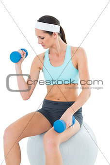 Fit woman exercising with dumbbells on fitness ball