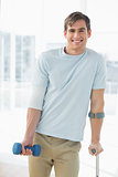 Smiling young man with crutch and dumbbell