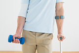 Mid section of a young man with crutch and dumbbell