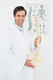 Smiling male doctor holding skeleton model in office