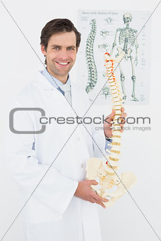 Smiling male doctor holding skeleton model in office