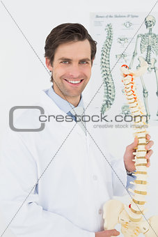 Smiling doctor holding skeleton model in office
