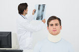 Patient in surgical collar with doctor examining spine x-ray behind