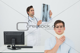 Patient in surgical collar while doctor examining spine x-ray behind