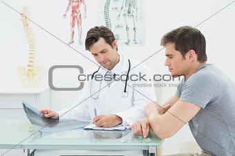 Male doctor writing reports besides patient