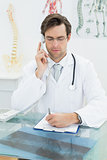 Serious male doctor using telephone at office