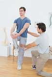 Male therapist assisting young man with stretching exercises