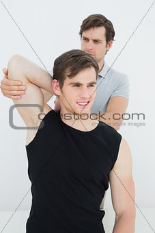 Male physiotherapist stretching a smiling young mans arm