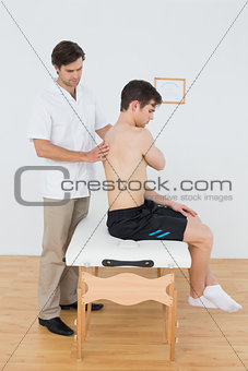 Shirtless man being examined by a physiotherapist in office