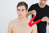 Physiotherapist putting red kinesio tape on patients shoulder