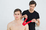 Physiotherapist putting on red kinesio tape on patients shoulder