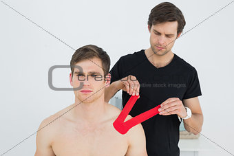 Physiotherapist putting on red kinesio tape on patients shoulder
