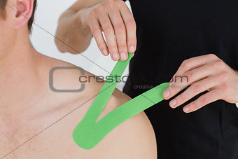 Physiotherapist putting on kinesio tape on patients shoulder