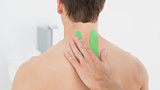 Physiotherapist putting on green kinesio tape on patients back