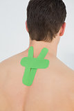 Rear view of a shirtless man with green kinesio tape on back