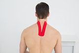Rear view of a shirtless man with kinesio tape on back