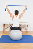 Rear view of a young man sitting on yoga ball
