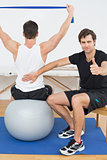 Therapist gestures thumbs up besides man on yoga ball