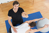 Therapist gesturing thumbs up by man with yoga ball