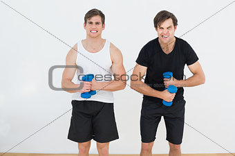 Two young men flexing muscles with dumbbells