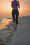 Closeup on fitness young woman running on beach in the evening