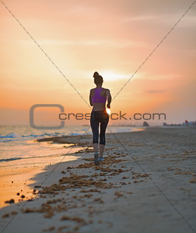 Fitness young woman running on beach in the evening. rear view