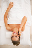Smiling young woman laying on massage table and talking cell pho