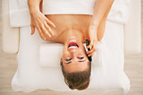 Happy young woman laying on massage table and talking cell phone