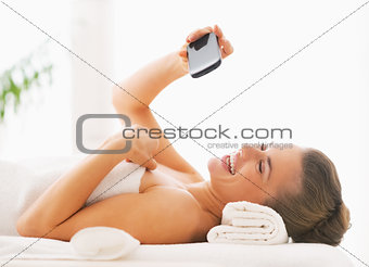 Happy young woman taking self photo while laying on massage tabl