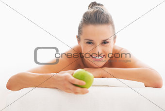 Young woman with apple laying on massage table