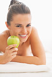 Portrait of happy young woman with apple laying on massage table