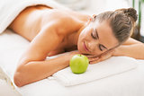 Relaxed young woman with apple laying on massage table