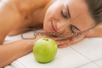 Relaxed young woman with apple laying on massage table