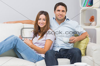 Cute couple sitting on sofa with tea cups at home