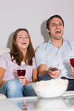 Happy couple with wine and popcorn enjoying a movie at home