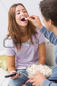 Cropped man feeding popcorn to a happy woman at home