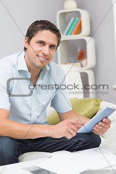 Smiling man with bills using digital tablet in the living room