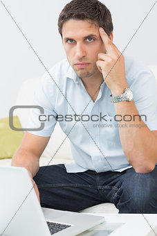 Portrait of serious man using laptop in living room