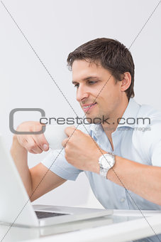Smiling young man with teacup using laptop at home