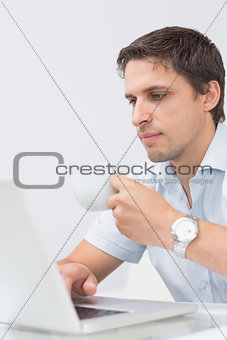 Serious man with teacup using laptop at home