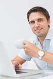 Smiling man with teacup using laptop at home
