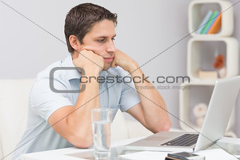 Serious young man using laptop in living room