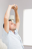 Man stretching up his hands with eyes closed in living room