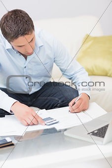 Young man with bills, calculator and laptop at home