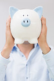 Casual man holding piggy bank in front of his face