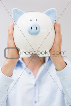 Casual man holding piggy bank in front of his face