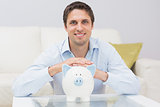 Handsome casual man with piggy bank in living room