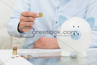 Mid section of a man putting some coins into a piggy bank