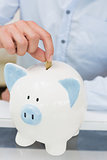 Close-up mid section of a man putting coin into piggy bank