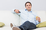 Man with a drink and remote control sitting on sofa at home